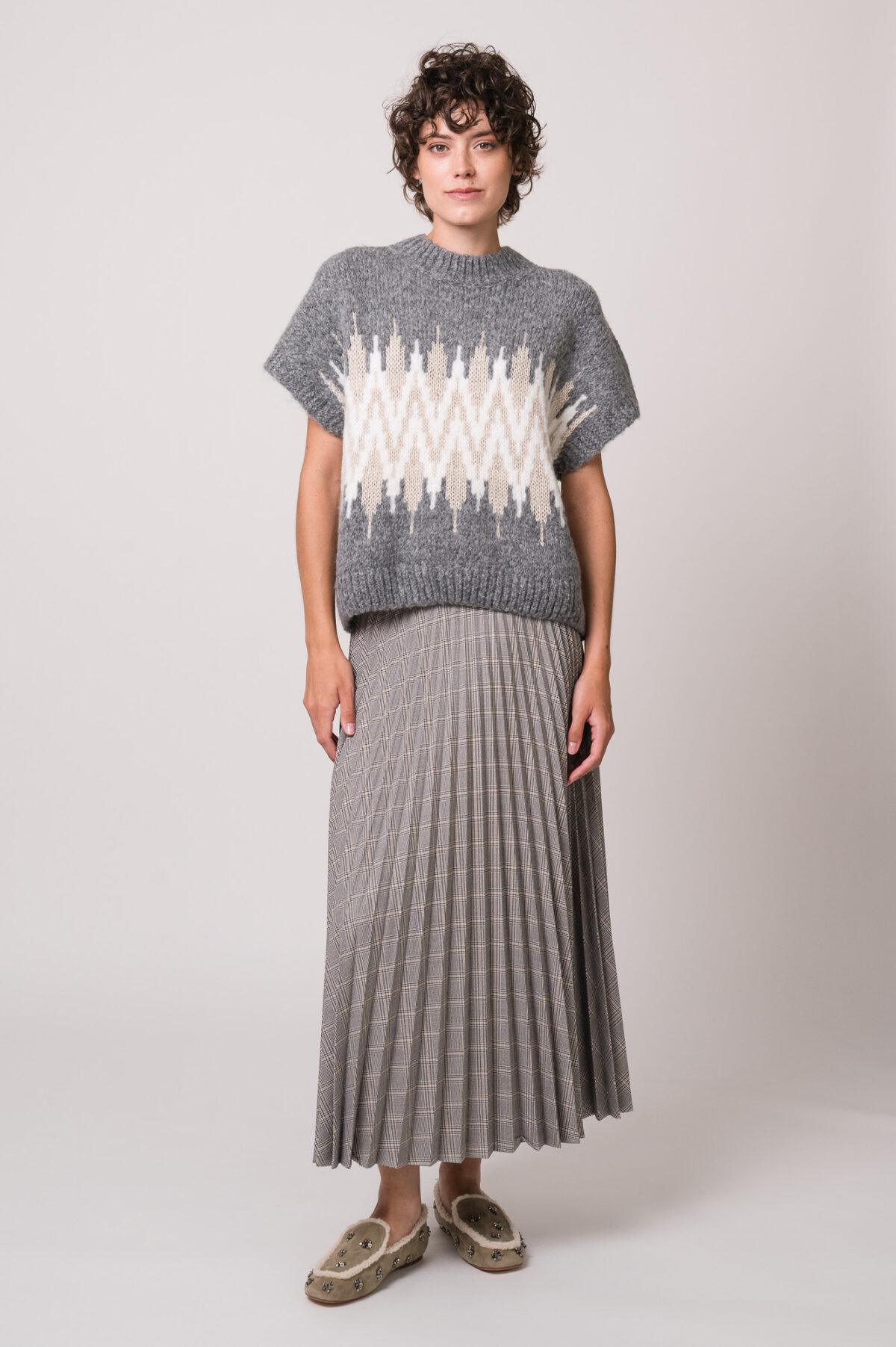 Model trägt einen grau gemusterten Kurzarm-Strickpullover und einen grau karierten Faltenrock der Marke Joop!
