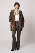 Model trägt eine braune Jacke der Marke Lou Andrea, eine natur-farbige Bluse der Marke The Mercer, eine dunkelbraune Hose der Marke Cambio und einen beigen Schal der Marke Mouleta.