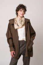 Model trägt eine braune Jacke der Marke Lou Andrea, eine natur-farbige Bluse der Marke The Mercer, eine dunkelbraune Hose der Marke Cambio und einen beigen Schal der Marke Mouleta.