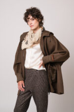 Model trägt eine braune Jacke der Marke Lou Andrea, eine natur-farbige Bluse der Marke The Mercer, eine dunkelbraune Hose der Marke Cambio und einen beigen Schal der Marke Mouleta.