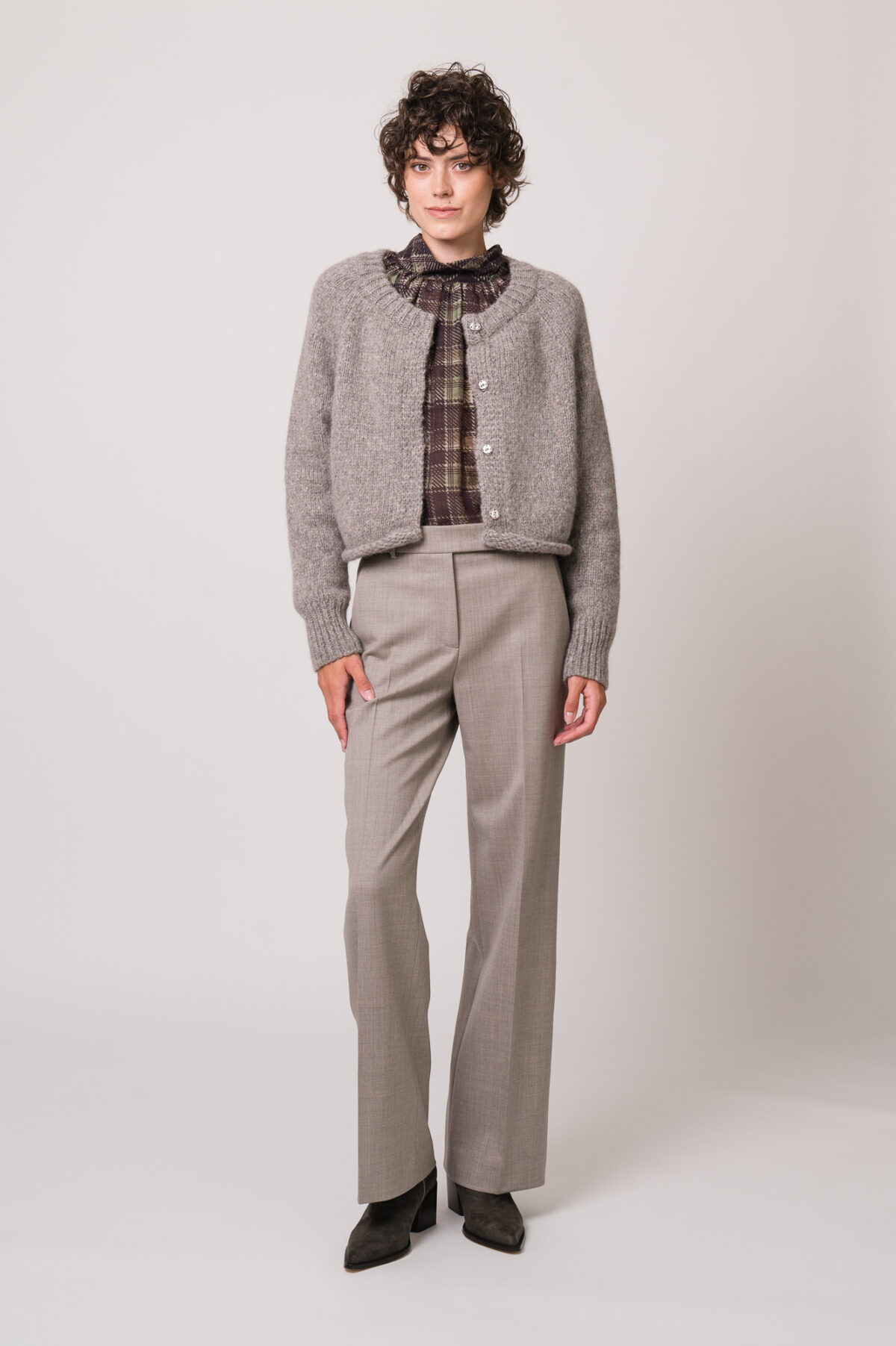 Model trägt eine graue Strickweste der Marke Susanne Bommer, eine braun-grün karierte Bluse der Marke SOSUE und eine graue Hose der Marke Quelle Due.