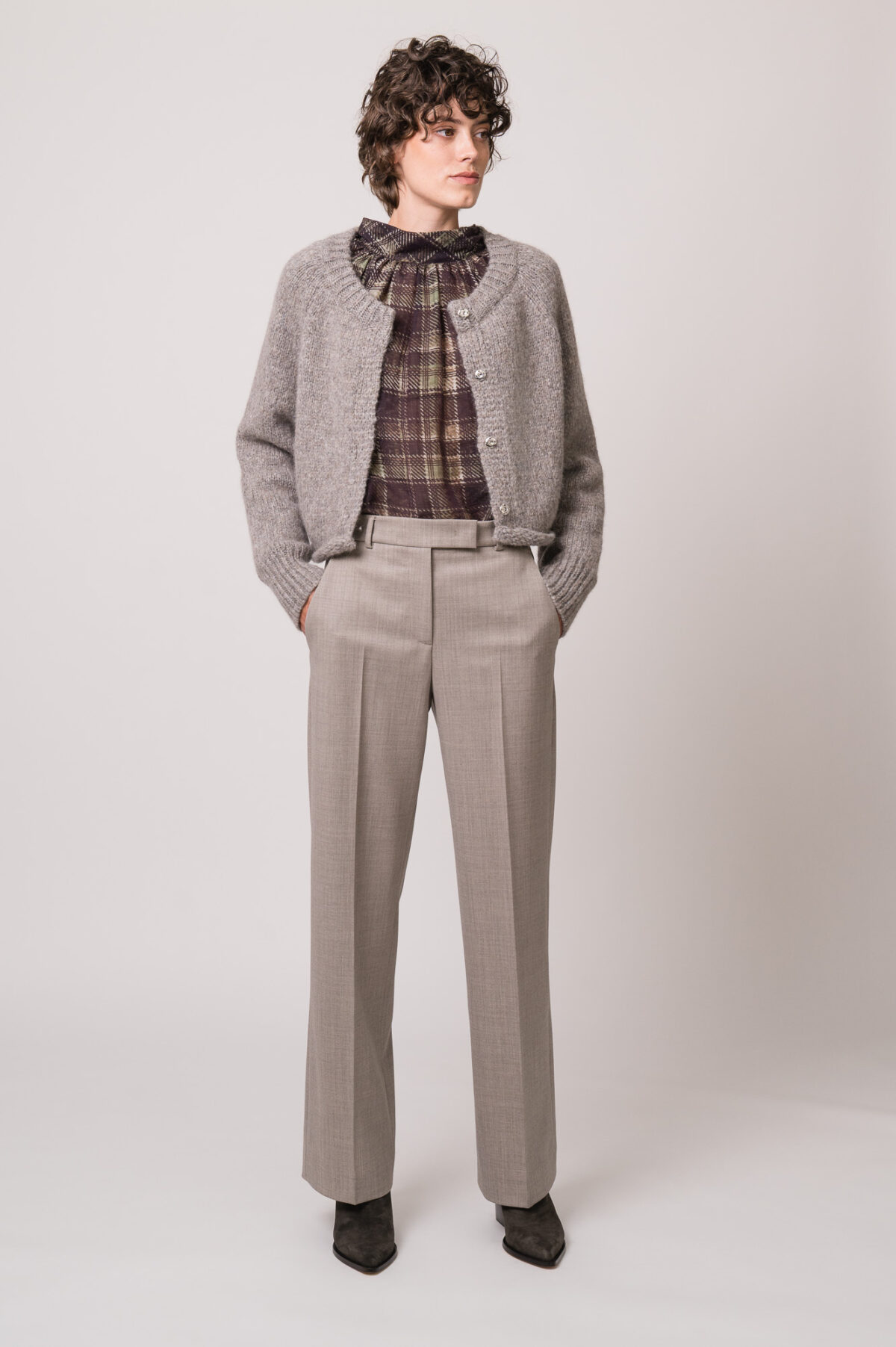 Model trägt eine graue Strickweste der Marke Susanne Bommer, eine braun-grün karierte Bluse der Marke SOSUE und eine graue Hose der Marke Quelle Due.
