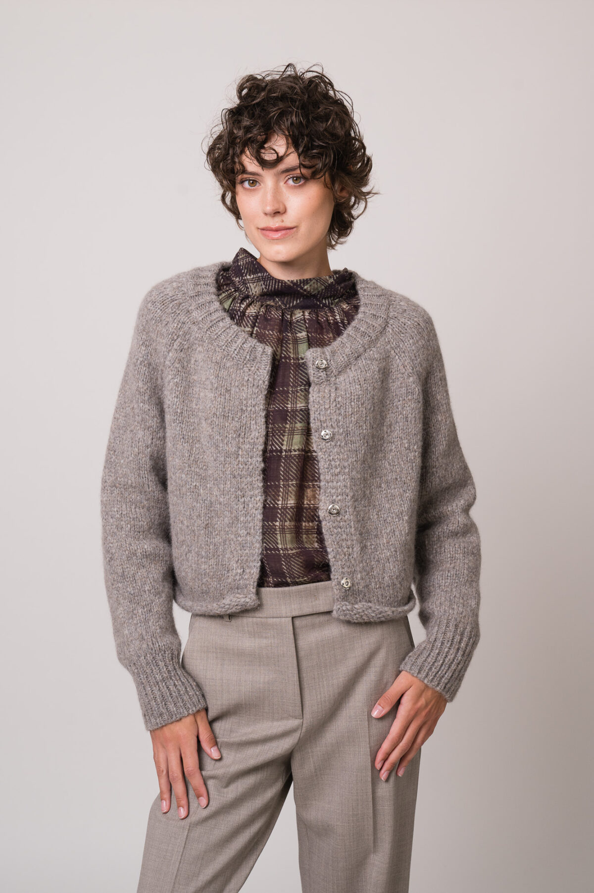 Model trägt eine graue Strickweste der Marke Susanne Bommer, eine braun-grün karierte Bluse der Marke SOSUE und eine graue Hose der Marke Quelle Due.