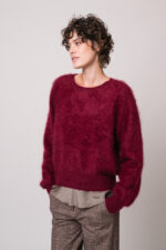 Model trägt einen weinroten Pullover der Marke Susanne Bommer und ein braunes Shirt der Marke Susanne Bommer.