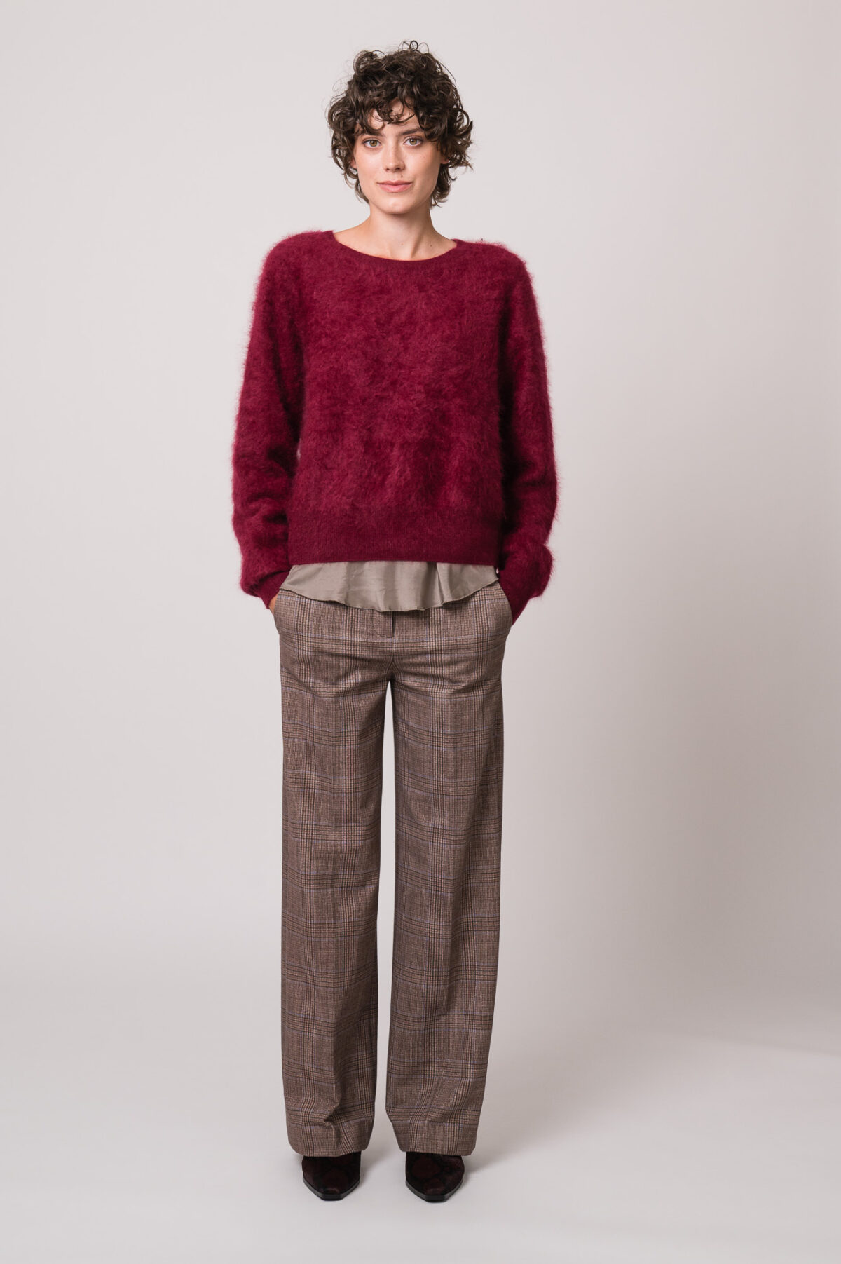 Model trägt einen weinroten Pullover der Marke Susanne Bommer, eine braun karierte Hose der Marke Circolo und ein braunes Shirt der Marke Susanne Bommer.