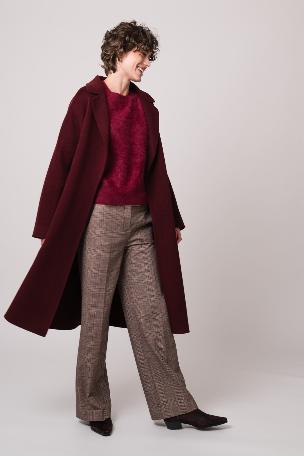 Model trägt einen weinroten Mantel der Marke Lu Li Lina, einen weinroten Pullover der Marke Susanne Bommer, eine braun karierte Hose der Marke Circolo.