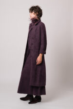 Model trägt einen Strickmantel, einen Pullover und einen Rock in violett der Marke FFC sowie einen Federschmuck der Marke Susanne Bommer.