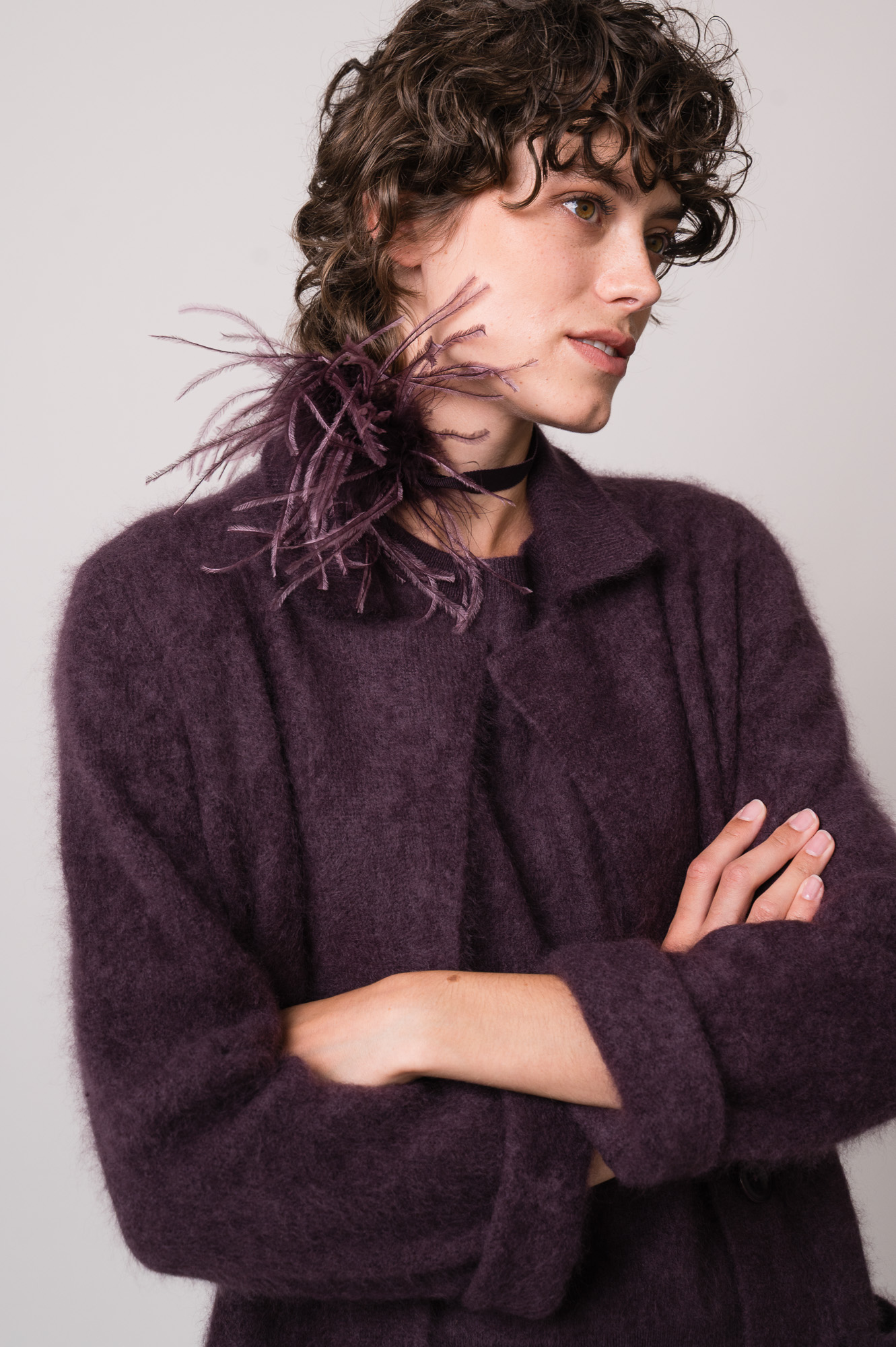 Model trägt einen Strickmantel und einen Pullover in violett der Marke FFC sowie einen Federschmuck der Marke Susanne Bommer.