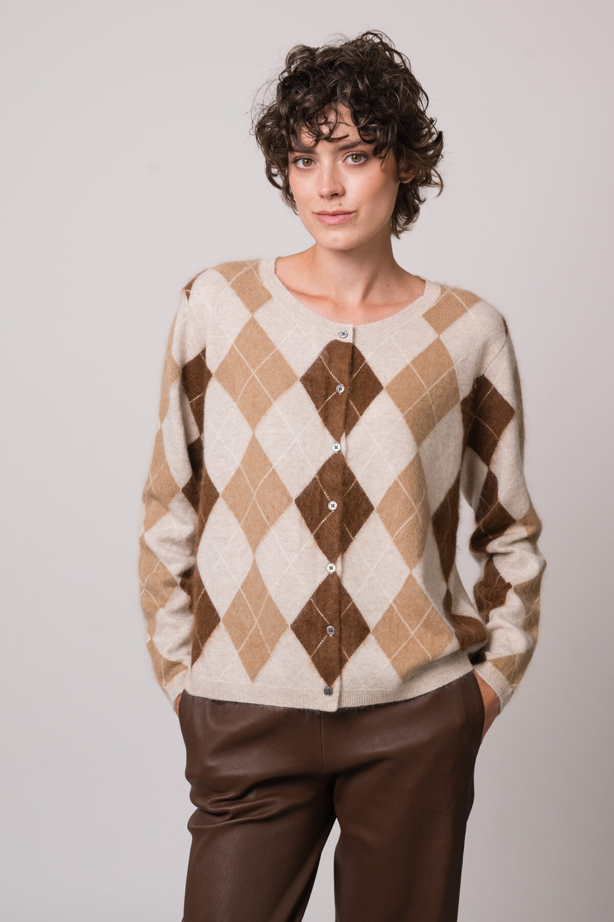 Model trägt eine beige Strickweste mit Rautenmuster der Marke The Mercer.