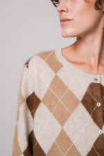 Model trägt eine beige Strickweste mit Rautenmuster der Marke The Mercer.