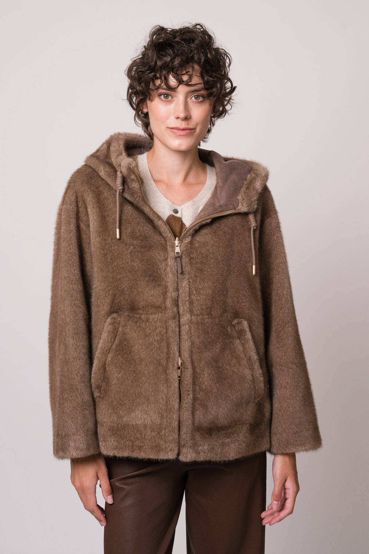 Model trägt eine beide Fake Fur Jacke der Marke Mabrun, eine beige Strickweste mit Rautenmuster der Marke The Mercer.