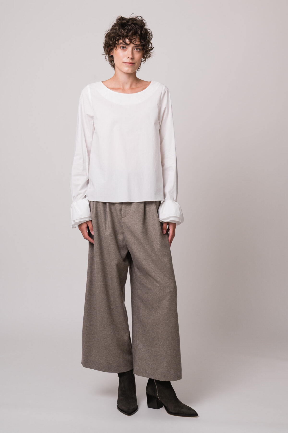 Model trägt eine weiße Bluse und eine beige Hose der Marke Susanne Bommer.