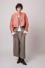 Model trägt eine rosa-goldene Jacke, eine beige Weste, eine weiße Bluse und eine beige Hose der Marke Susanne Bommer.