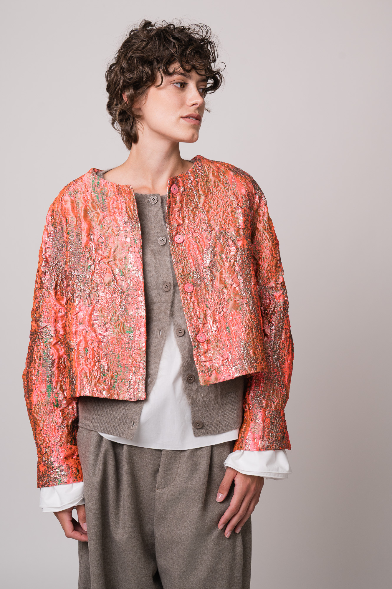 Model trägt eine rosa-goldene Jacke, eine beige Weste, eine weiße Bluse und eine beige Hose der Marke Susanne Bommer.