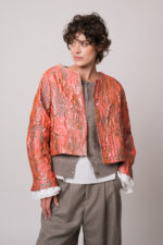 Model trägt eine rosa-goldene Jacke, eine beige Weste, eine weiße Bluse und eine beige Hose der Marke Susanne Bommer.