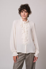 Model trägt eine natur-farbige Bluse mit Vollant und eine beige Hose der Marke Lis Lareida.