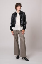 Model trägt eine schwarze Lederjacke, eine natur-farbige Bluse mit Vollant und eine beige Hose der Marke Lis Lareida.