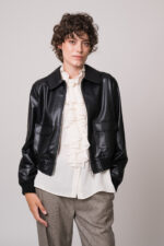 Model trägt eine schwarze Lederjacke, eine natur-farbige Bluse mit Vollant und eine beige Hose der Marke Lis Lareida.