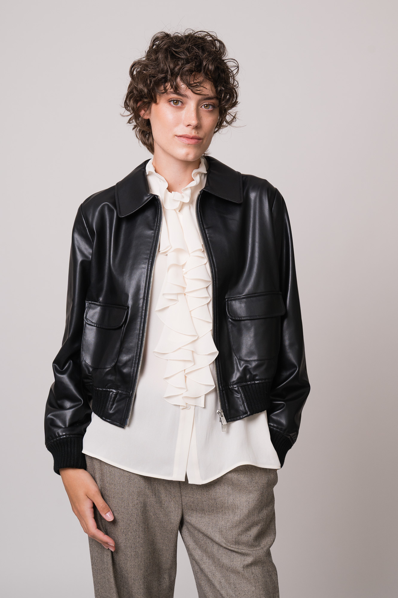 Model trägt eine schwarze Lederjacke, eine natur-farbige Bluse mit Vollant und eine beige Hose der Marke Lis Lareida.