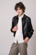 Model trägt eine schwarze Lederjacke, eine natur-farbige Bluse mit Vollant und eine beige Hose der Marke Lis Lareida.