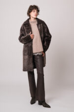 Model trägt einen braunen Lammfellmantel von Hemisphere, eine beiges Top mit Spitze der Marek Allude, einen beigen Pullover der Marke Hemisphere, eine braune Jeans der Marke 7 for all mankind.