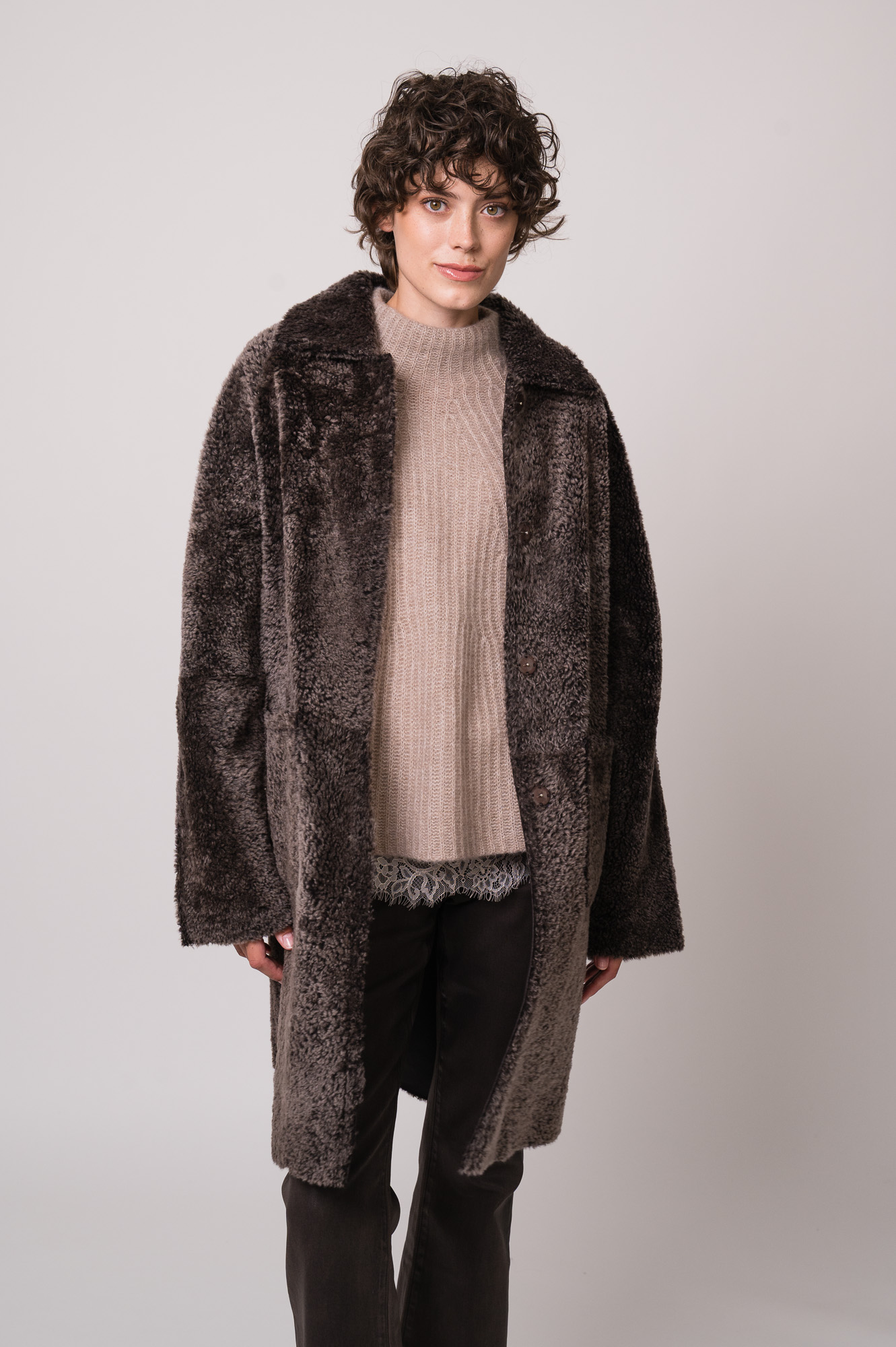 Model trägt einen braunen Lammfellmantel von Hemisphere, eine beiges Top mit Spitze der Marek Allude, einen beigen Pullover der Marke Hemisphere, eine braune Jeans der Marke 7 for all mankind.