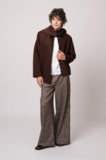 Model trägt eine dunkelbraune Jacke der Marke Luisa Cerano, eine weiße Bluse der Marke Soluzione, eine braun karierte Hose der Marke Cambio.