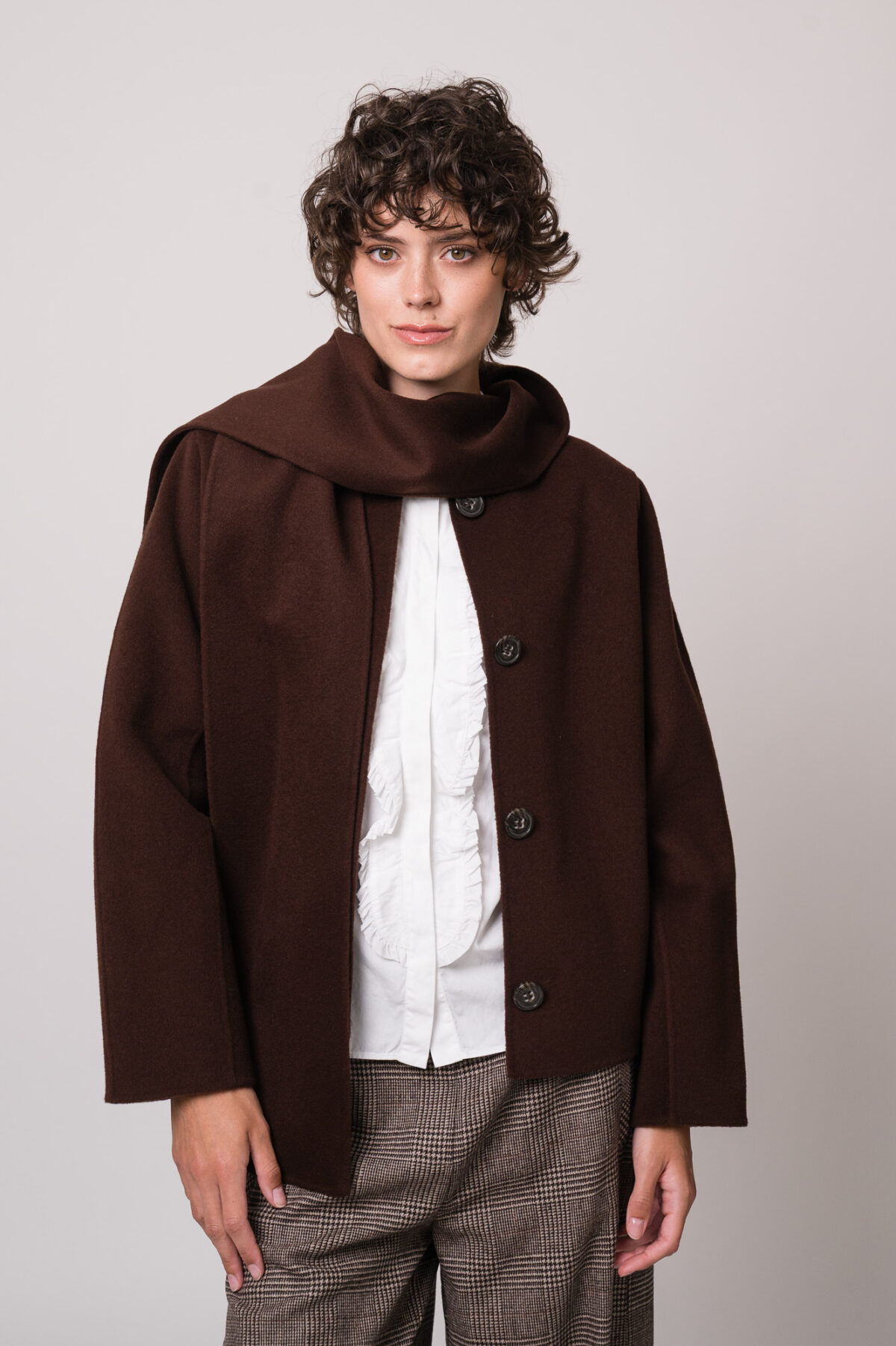 Model trägt eine dunkelbraune Jacke der Marke Luisa Cerano, eine weiße Bluse der Marke Soluzione, eine braun karierte Hose der Marke Cambio.
