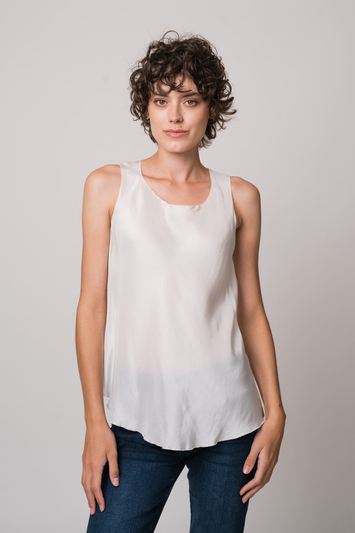 Model trägt ein weißes Seidentop der Marke Susanne Bommer, eine blaue Jeans der Marke 7 for all mankind.