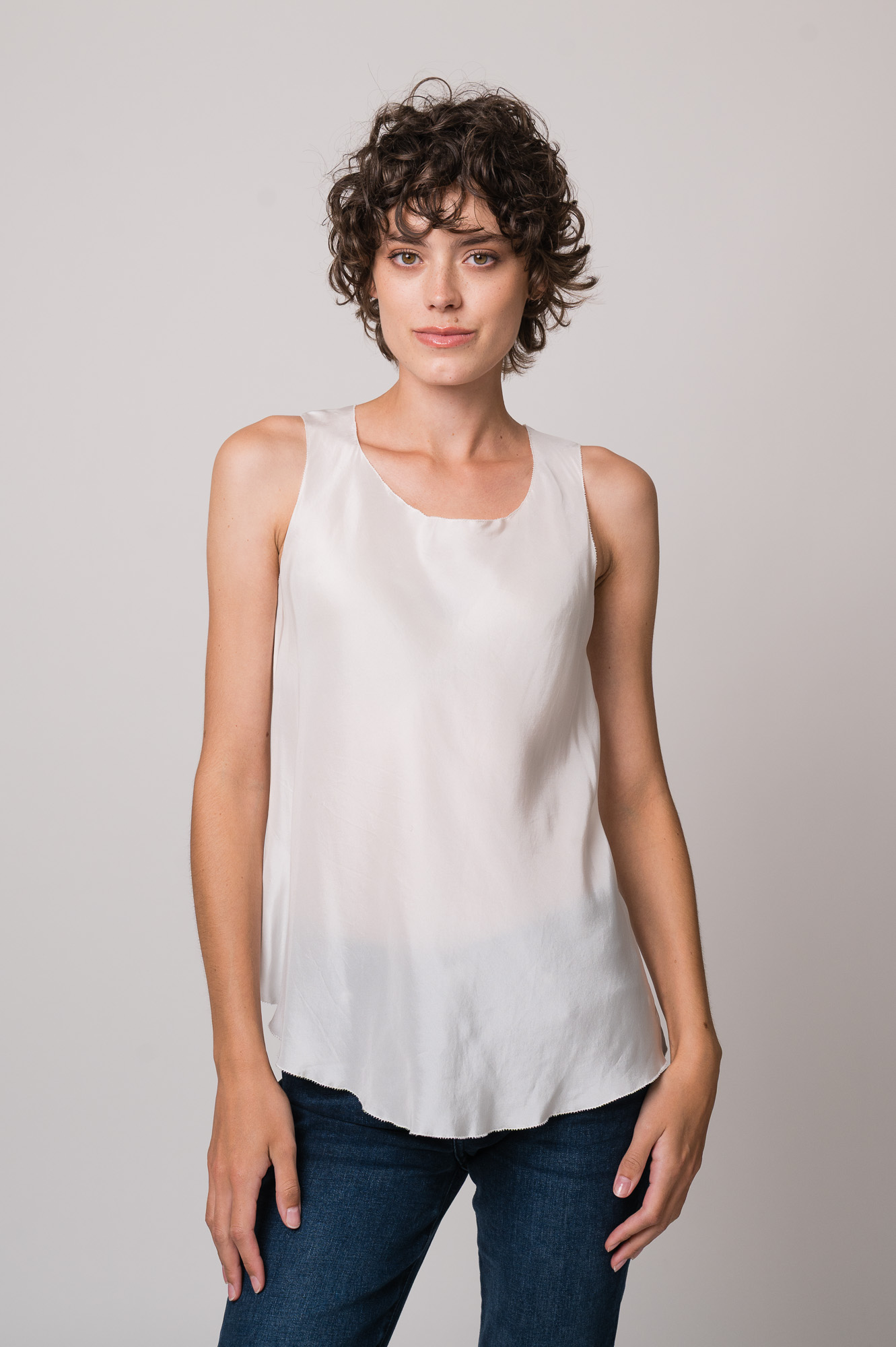 Model trägt ein weißes Seidentop der Marke Susanne Bommer, eine blaue Jeans der Marke 7 for all mankind.