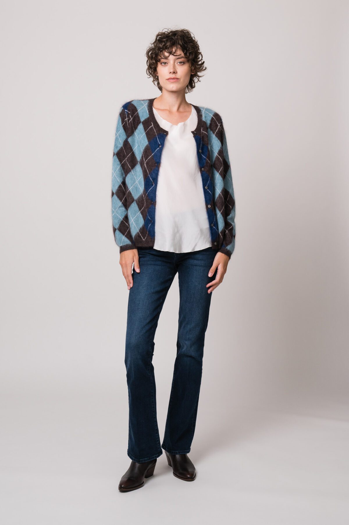 Model trägt eine blau-braune Weste mit Rautenmuster der Marke The Mercer, ein weißes Seidentop der Marke Susanne Bommer, eine blaue Jeans der Marke 7 for all mankind.
