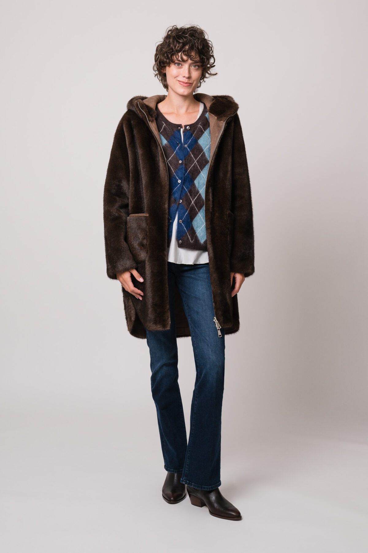 Model trägt eine braune Jacke der Marke Betta Corradi, eine blau-braune Weste mit Rautenmuster der Marke The Mercer, ein weißes Seidentop der Marke Susanne Bommer, eine blaue Jeans der Marke 7 for all mankind.