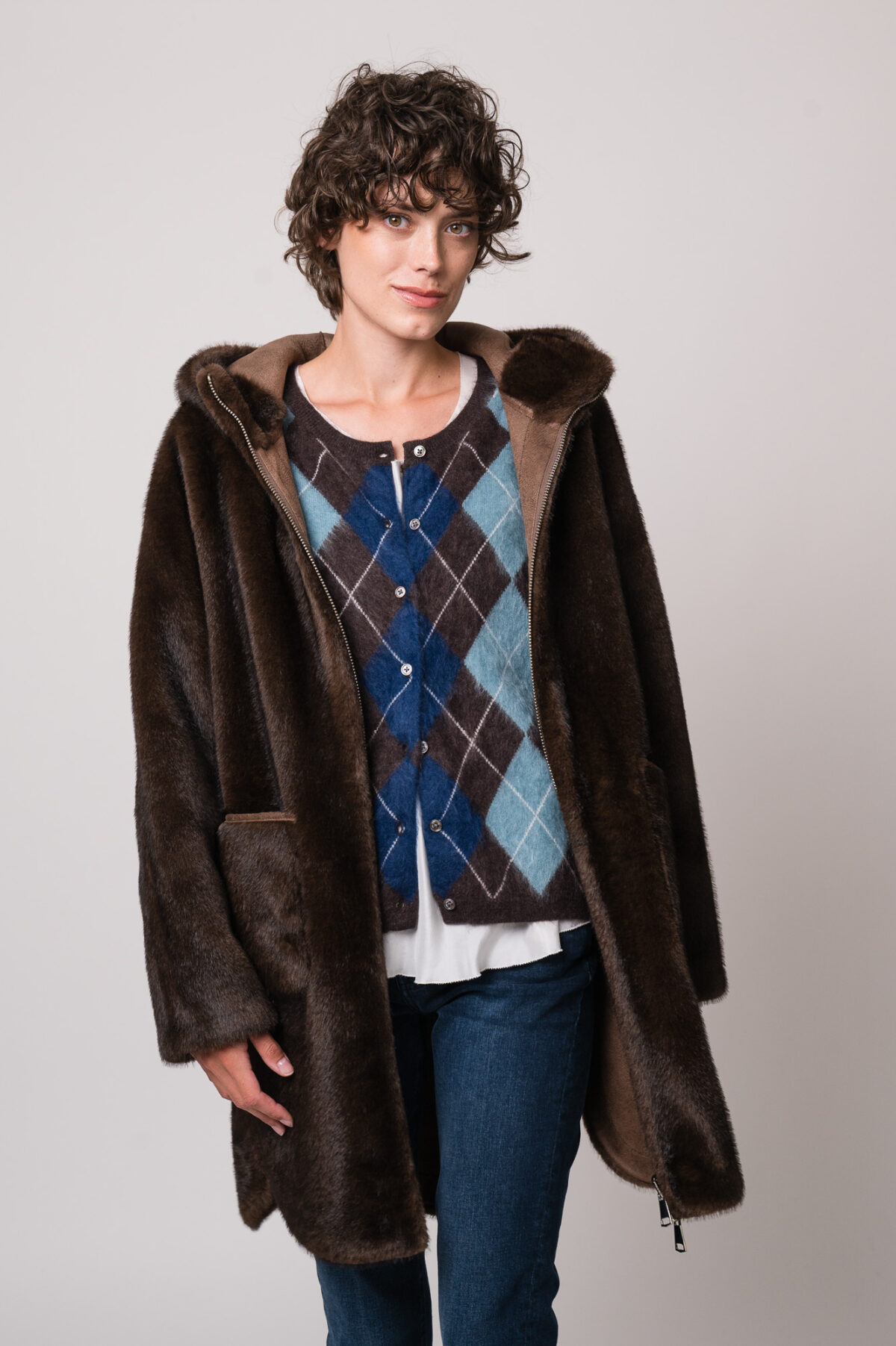 Model trägt eine braune Jacke der Marke Betta Corradi, eine blau-braune Weste mit Rautenmuster der Marke The Mercer, ein weißes Seidentop der Marke Susanne Bommer, eine blaue Jeans der Marke 7 for all mankind.