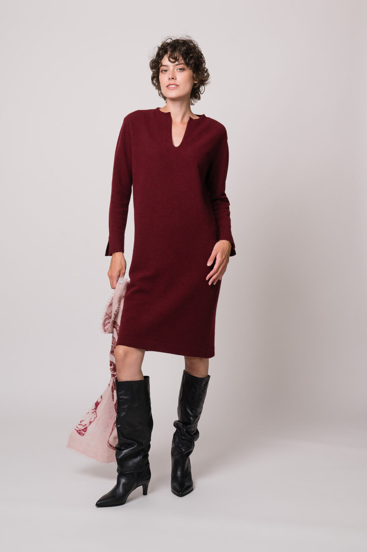 Model trägt ein weinrotes Strickkleid der Marke Rosso35 und eine rosa gemustertes Tuch der Marke Mouleta.