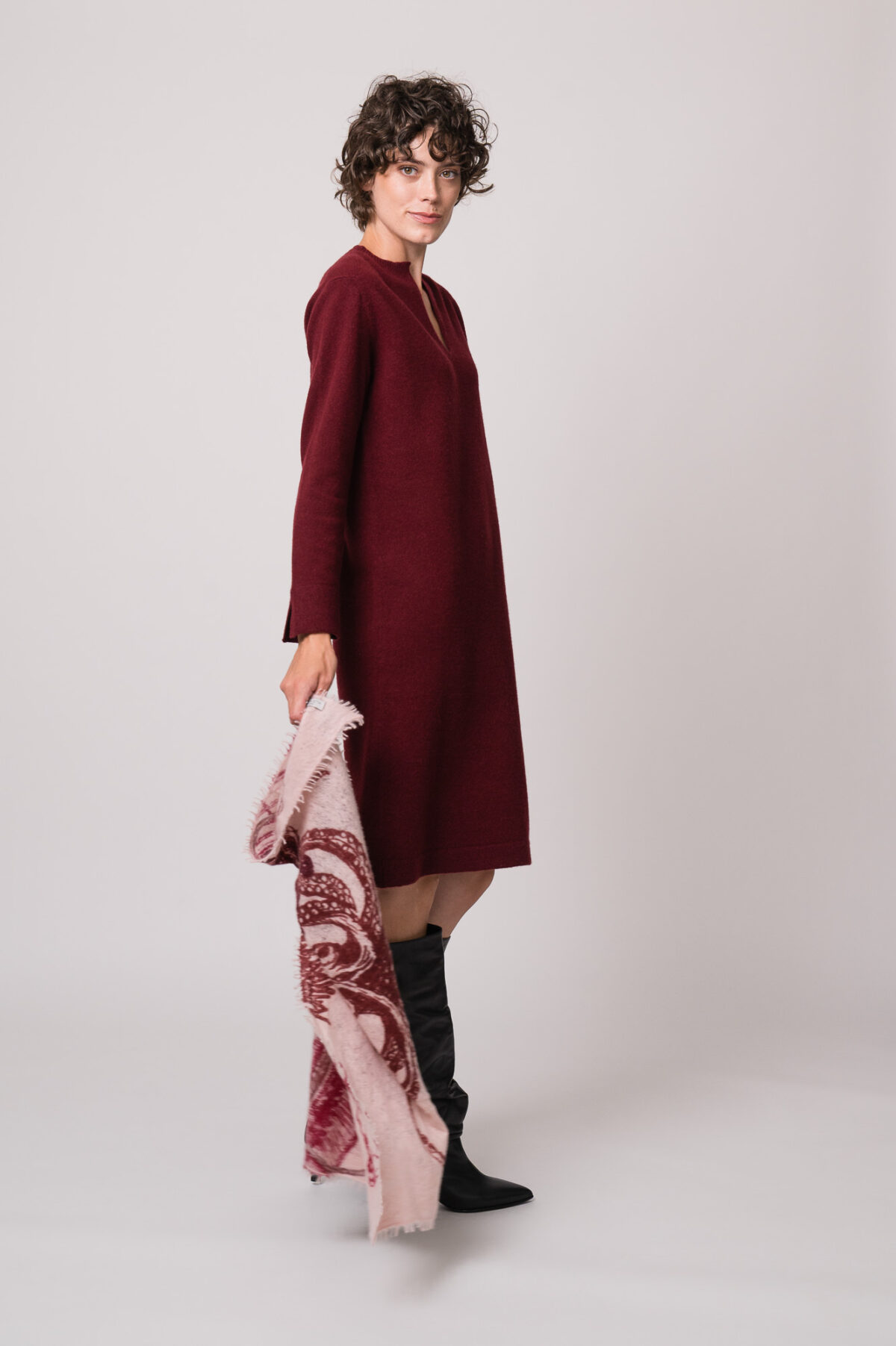 Model trägt ein weinrotes Strickkleid der Marke Rosso35 und eine rosa gemustertes Tuch der Marke Mouleta.