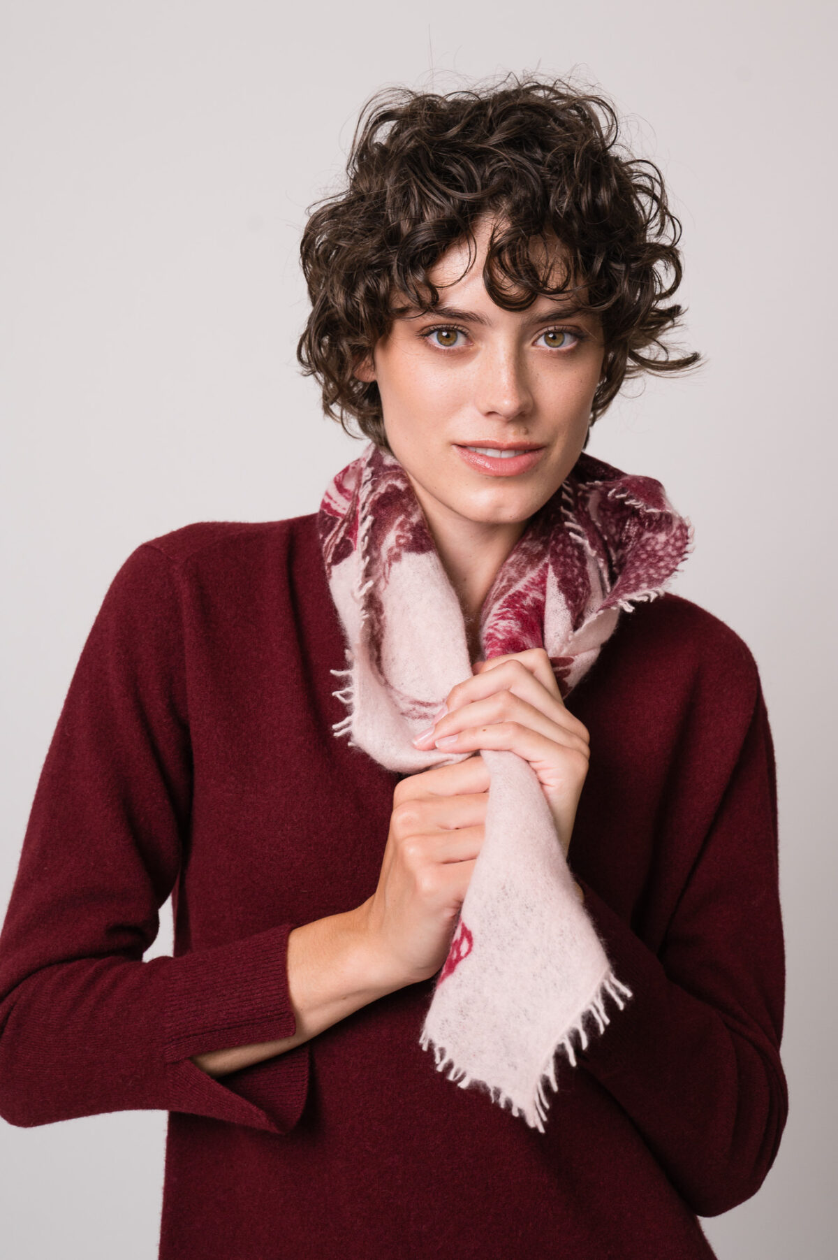Model trägt ein weinrotes Strickkleid der Marke Rosso35 und eine rosa gemustertes Tuch der Marke Mouleta.