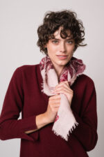 Model trägt ein weinrotes Strickkleid der Marke Rosso35 und eine rosa gemustertes Tuch der Marke Mouleta.