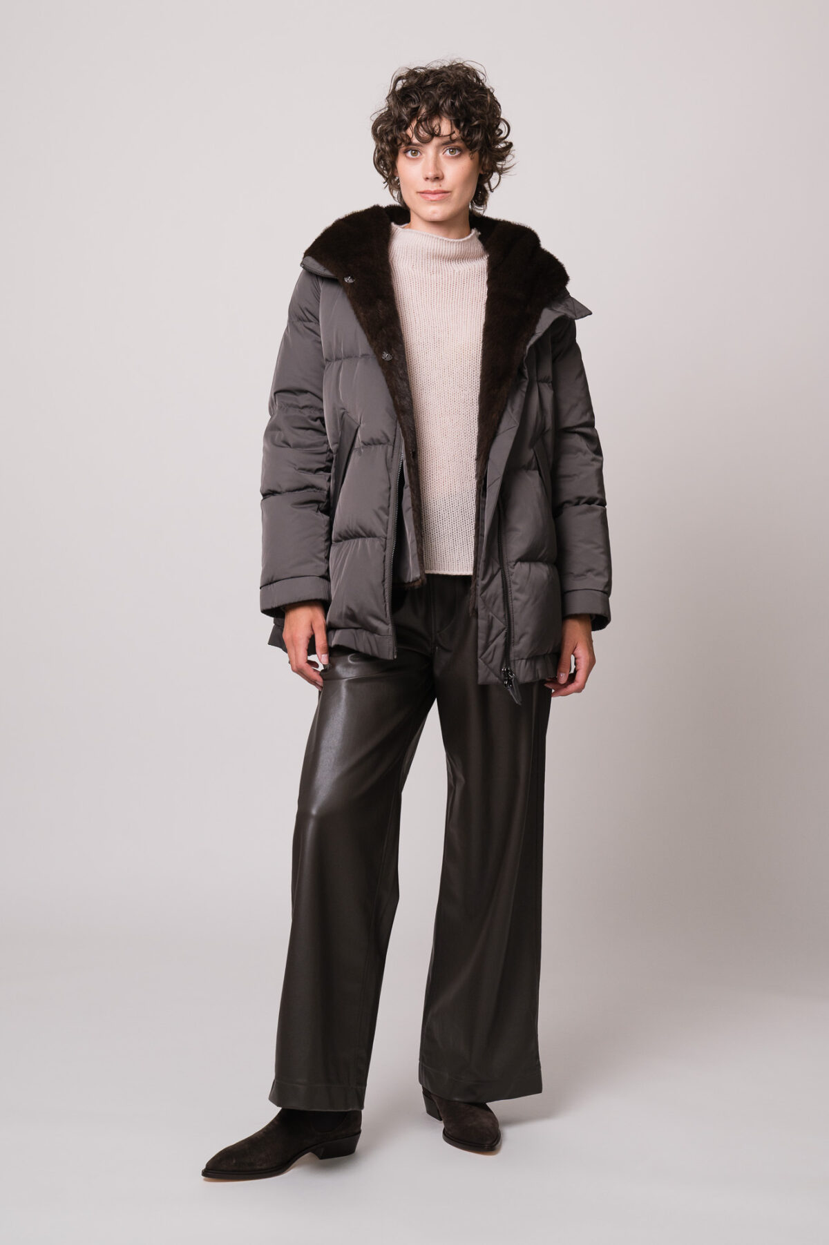 Model trägt eine dunkle Jacke der Marke Lou Andrea, einen natur-farbigen Pullover der Marke FFC und eine braune Hose der Marke Lis Lareida.