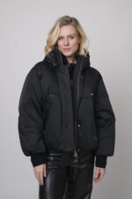 Das Model trägt eine schwarze Daunenjacke der Marke Duno sowie einen Lounge-Pullover von Unartig mit einem Motiv und eine schwarze Hose von Cambio.
