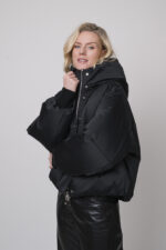 Das Model trägt eine schwarze Daunenjacke der Marke Duno sowie einen Lounge-Pullover von Unartig mit einem Motiv und eine schwarze Hose von Cambio.