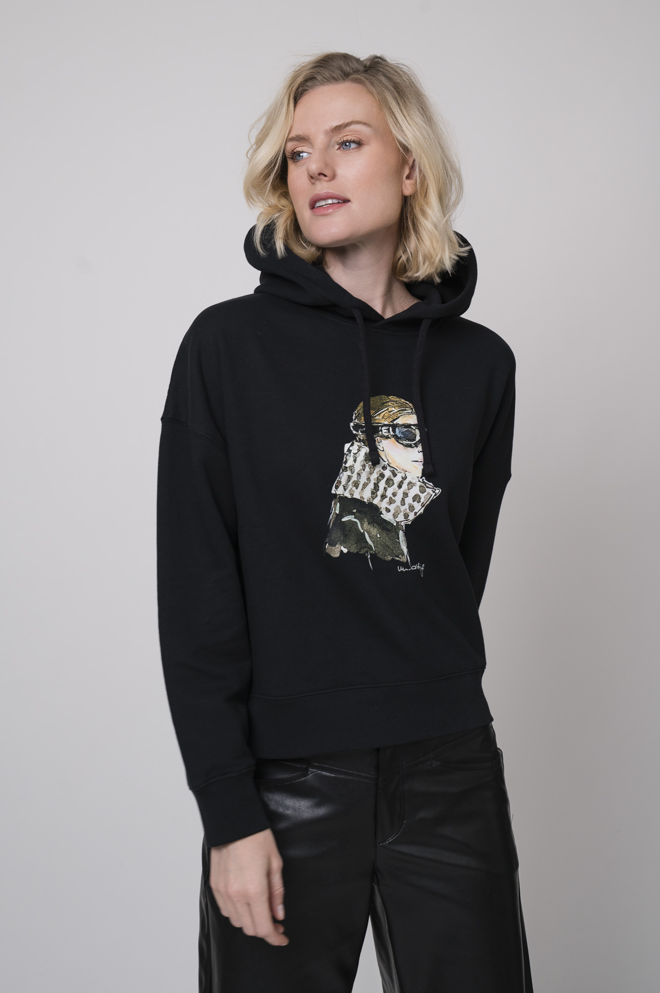 Das Model trägt einen Lounge-Pullover der Marke Unartig mit einem Motiv sowie eine Hose von Cambio in Schwarz.