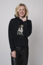 Das Model trägt einen Lounge-Pullover der Marke Unartig mit einem Motiv sowie eine Hose von Cambio in Schwarz.