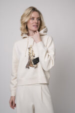 Das Model trägt einen Lounge-Pullover der Marke Unartig mit einem Motiv sowie eine Hose von Cambio in Natur.
