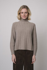 Das Model trägt einen Stehkragenpullover von Hemisphere in Sand, dazu eine Hose in braun von Cambio.