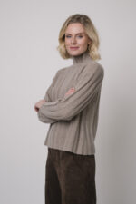 Das Model trägt einen Stehkragenpullover von Hemisphere in Sand, dazu eine Hose in braun von Cambio.