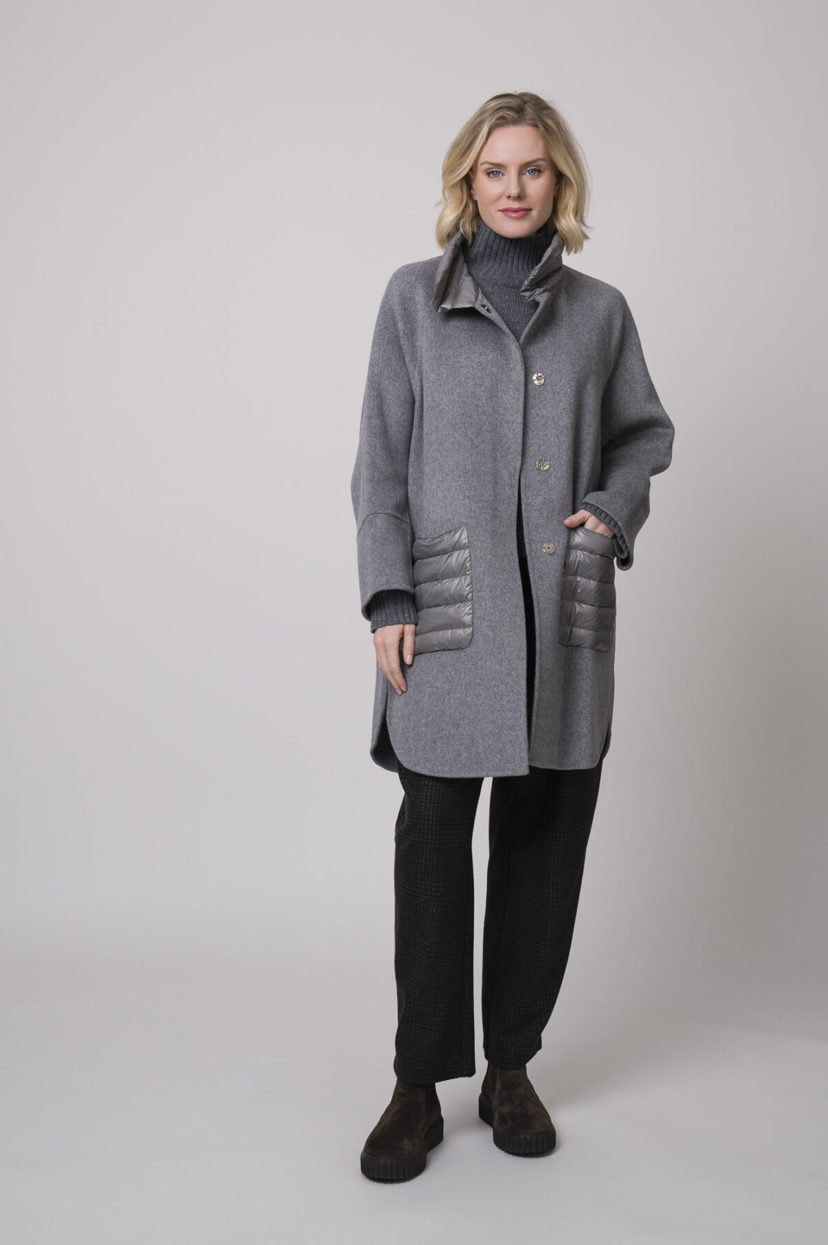 Das Model trägt einen Stehkragenpullover von Luisa Cerano, eine anthrazitfarbene, karierte Hose von Cambio und eine mittelgraue Jacke von Helmur.