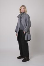 Das Model trägt einen Stehkragenpullover von Luisa Cerano, eine anthrazitfarbene, karierte Hose von Cambio und eine mittelgraue Jacke von Helmur.