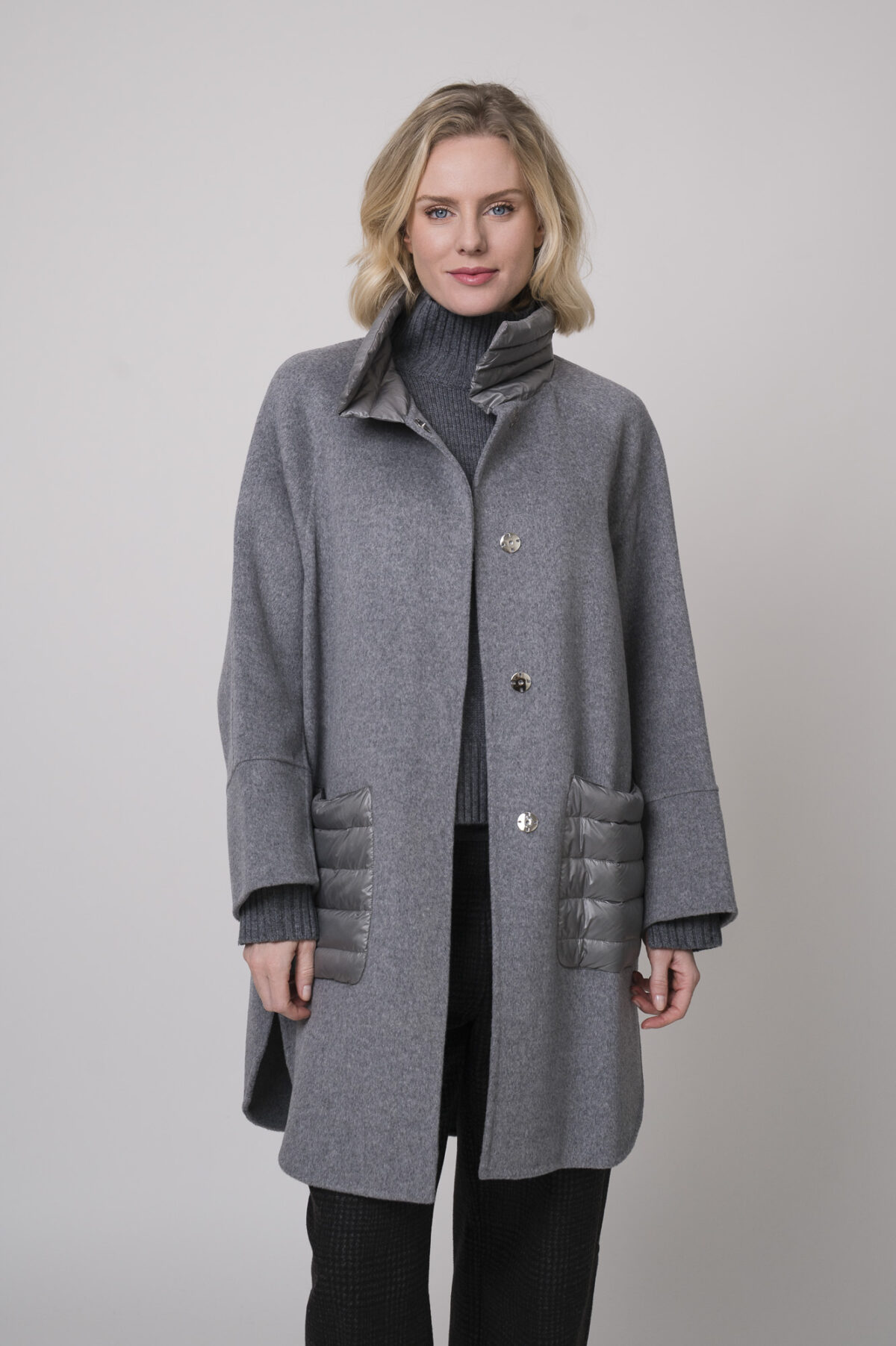 Das Model trägt einen Stehkragenpullover von Luisa Cerano, eine anthrazitfarbene, karierte Hose von Cambio und eine mittelgraue Jacke von Helmur.