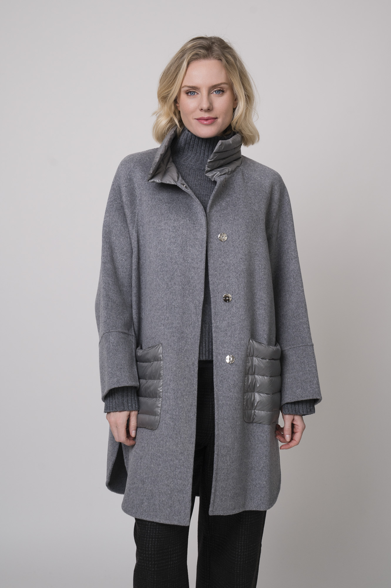 Das Model trägt einen Stehkragenpullover von Luisa Cerano, eine anthrazitfarbene, karierte Hose von Cambio und eine mittelgraue Jacke von Helmur.