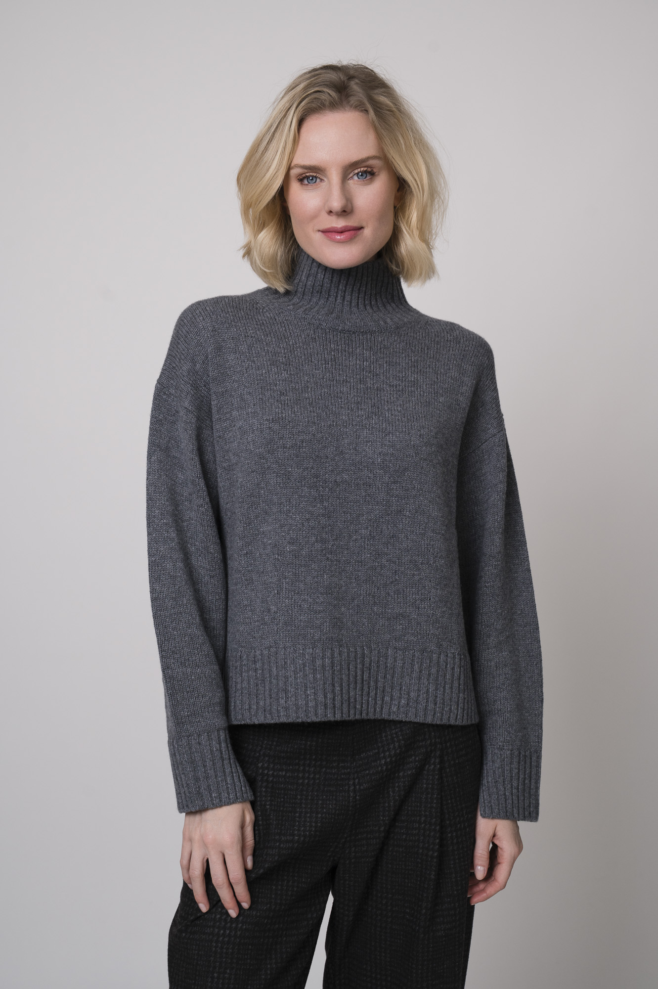 Das Model trägt einen Stehkragenpullover von Luisa Cerano und eine anthrazitfarbene, karierte Hose von Cambio.